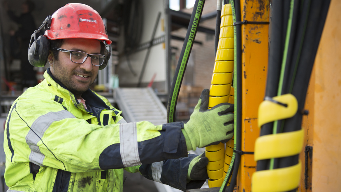 På bilden syns en man med arbetskläder. Han har på sig hjälm med hörselskydd, varselklädsel samt handskar. Han håller i ett tjockt rör.