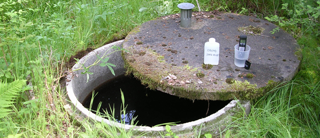 En brunn med ett öppoet lock. På locket står det provflaskor.