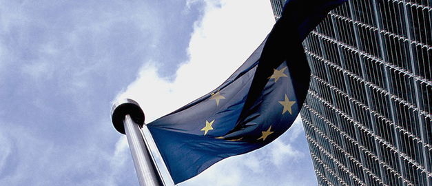 Översta delen av en blå EU-flagga med gula stjärnor på en flaggstång utanför Kommissionens högkvarter i Bryssel.
