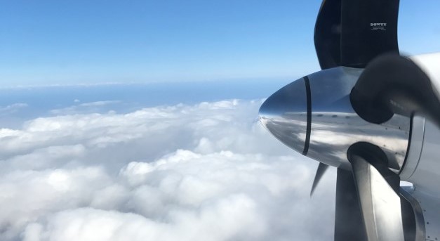 Närbild av en propeller till ett flygplan. I bakgrunden syns himmel och moln. Foto.