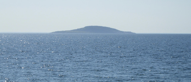 Vatten och i horisonten syns en ö. Foto.