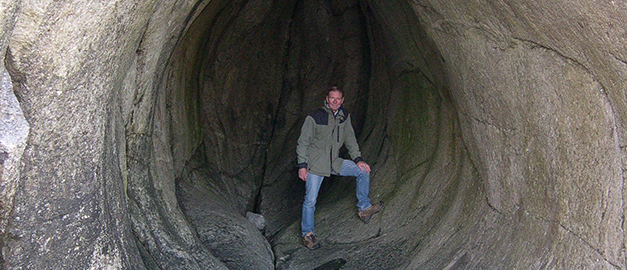 En man står i öppningen till en så kallad lökgrotta. Härnökusten. Foto.