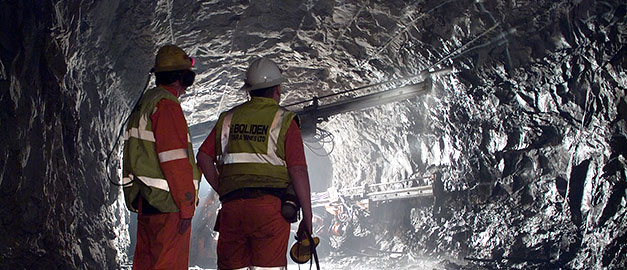 Bilden visar en gång i en gruva. I förgrunden syns två män med arbetskläder.