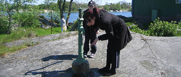 På bilden syns en kvinna som dricker vatten ur sina händer. Vattnet kommer från en egen borrad dricksvattenbrunn. Bakom kvinnan syns en pojke.